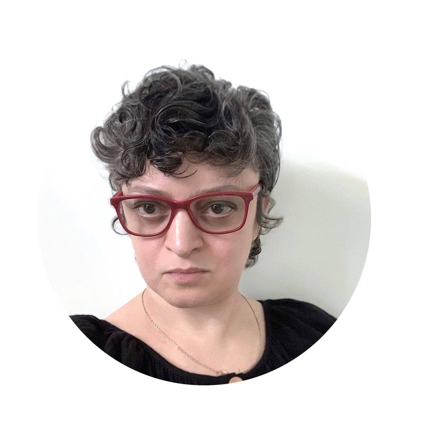 Katya Grokhovsky with black shirt & red glasses looking directly at the camera.